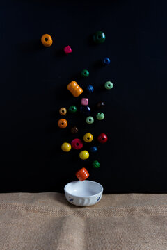 White bowl on a table with colored wooden beads in the air on black background 
