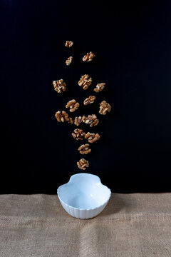 White bowl on a table with walnuts in the air on black background