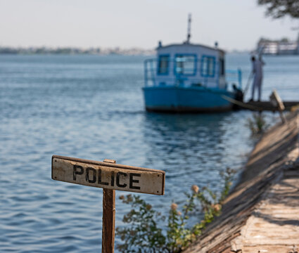 Small steel motor launch boat moored on the Nile river bank with rope mooring line and police wooden sign in foreground