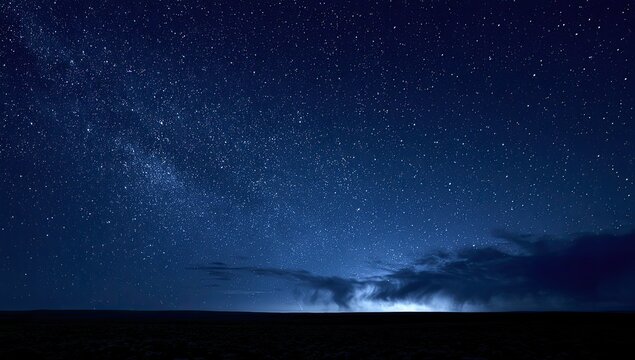 Vast, star-dusted night sky above a dark horizon with distant, faint light