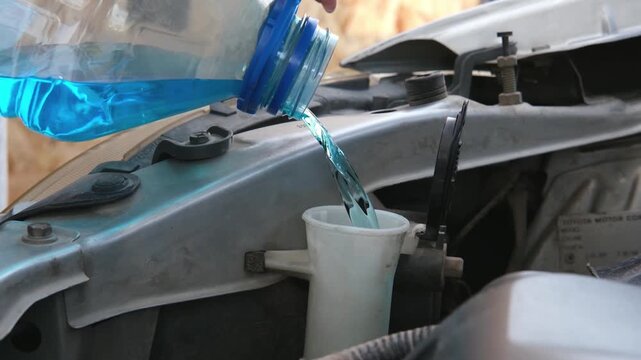 Woman hand filling car reservoir with wiper fluid using whole bottle of antifreeze fluid