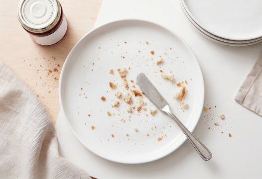 Top view of an empty white breakfast plate with scattered bread crumbs and a table knife.