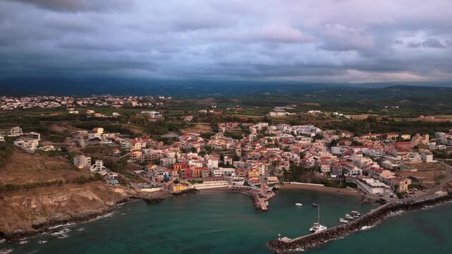 Aerial drone view of the harbor and breakwater of a colorful coastal village with red-roofed houses, Panormos, Greece