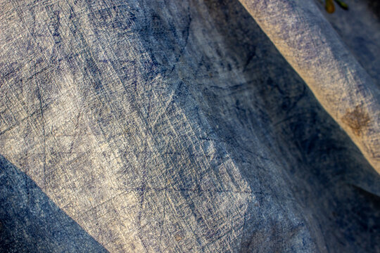 Close up detail of bluish gray woven plastic tarpaulin fold texture protecting outdoor goods.