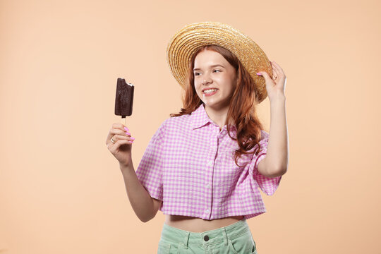Happy teenage girl with delicious chocolate-glazed ice cream on beige background