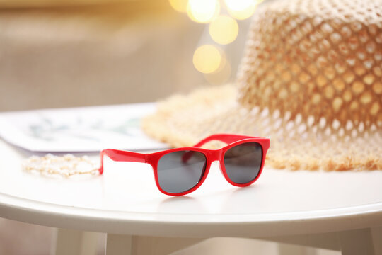 Stylish sunglasses, jewelry and straw hat on white table indoors, closeup