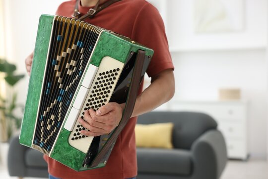 Man playing piano accordion at home, closeup. Space for text