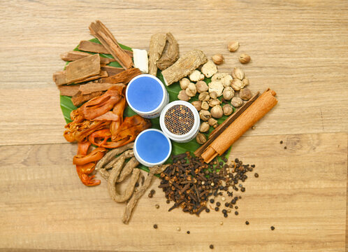 Top view of traditional Thai herbal ingredients for inhalers, including cloves, borneol, menthol, nutmeg, agarwood, black pepper, and camphor, arranged on a rustic wooden background,