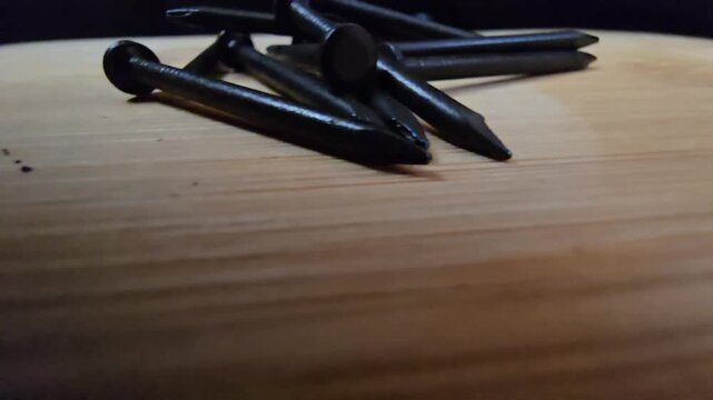 Close-up of black iron nails arranged on a clean wooden surface. High-quality macro shot showcasing construction materials and hardware tools for DIY, carpentry, or industrial renovation projects.