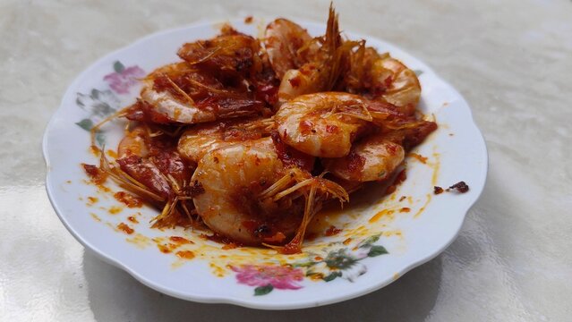 Close-up of spicy fried shrimp with red chili paste (udang balado) served on a floral plate, representing authentic Indonesian home cooking and traditional Asian seafood cuisine.