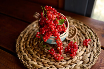 Obraz premium Fresh red currants in a blue and white bowl on a woven mat in a wooden setting