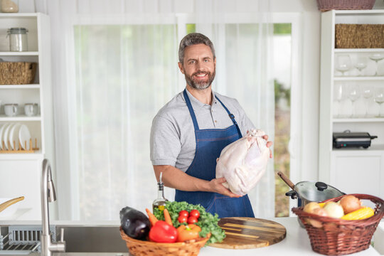 Cooking turkey for Thanksgiving. Man in apron with turkey. Home menu. Thanksgiving day dinner. Chef man cooking in kitchen. Thanksgiving dinner food. Man cooking preparing food