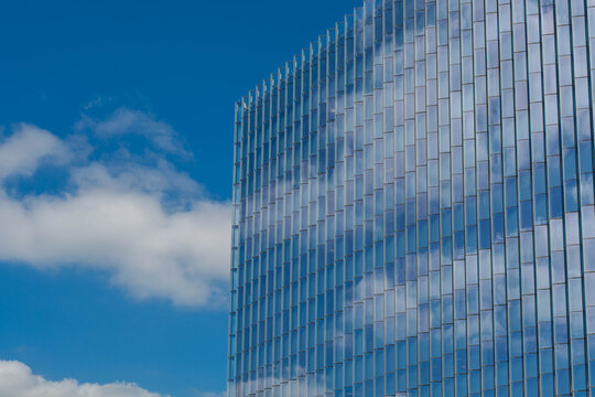 Abstract architectural detail of a glass skyscraper facade reflecting a blue sky with fluffy white clouds.