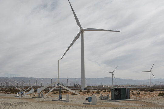 Close up view of a large clean wind turbine standing in a desert field with older disassembled turbine parts on the ground.