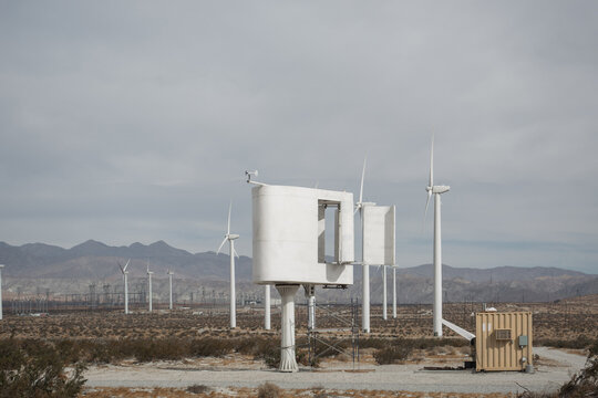 An innovative white vertical axis wind turbine prototype standing in a desert landscape next to traditional wind generators.