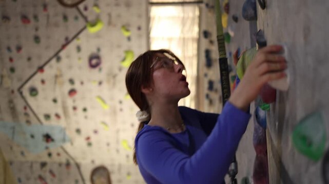 Indoor rock climbing training pauses as a woman catches her breath on the climbing wall after a demanding section while building endurance and resilience
