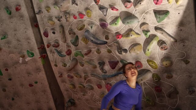 Young woman loses grip from fatigue and drops from low climbing wall during training showing physical exhaustion limits and realistic struggle in bouldering session