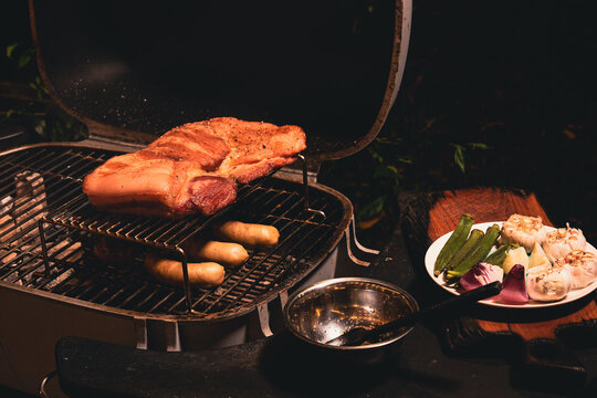 Barbecue grill meat sausage vegetable plate outdoor cooking scene with seasoned pork skewer bowl and warm firelight for rustic meal preparation