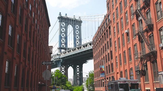 Scenic perspective of the Manhattan Bridge with brick buildings and lush greenery foreground
