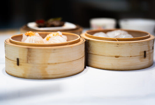 Traditional Chinese dim sum in bamboo steamers on white tablecloth, featuring shrimp dumplings and har gow, restaurant dining setting