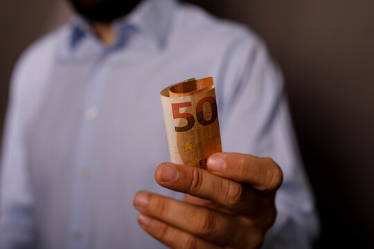 Hand holding a rolled fifty euro banknote, representing finance and wealth.