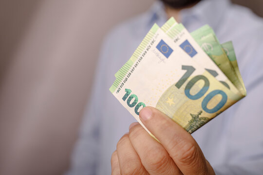 Close up view of a hand holding several folded 100 euro banknotes, showing financial transactions an