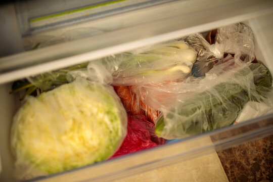 Open refrigerator vegetable drawer with fresh cabbage in plastic bag, greens and vegetables stored inside, cherries and strawberries visible above