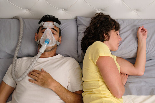 Man sleeping with CPAP machine while partner rests peacefully in bed