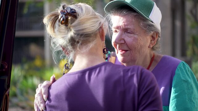 An elderly mother and her mature daughter embrace tightly while saying goodbye outside the home before the mother moves to a facility.