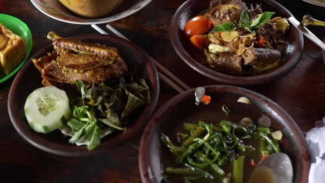 Traditional Indonesian dishes with fried chicken, braised meat, vegetables, and tofu served in rustic clay plates, authentic culinary footage.