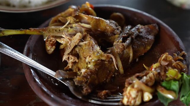 Traditional Indonesian braised chicken with rich spices and savory sauce, served on a rustic clay plate, close-up culinary footage.