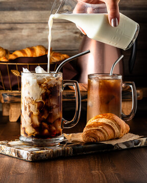 Pouring milk into a glass of iced coffee, served with croissants.