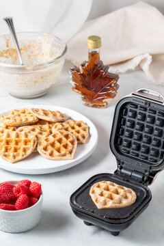 A mini waffle iron maker with heart shaped mini waffles, served with raspberries
