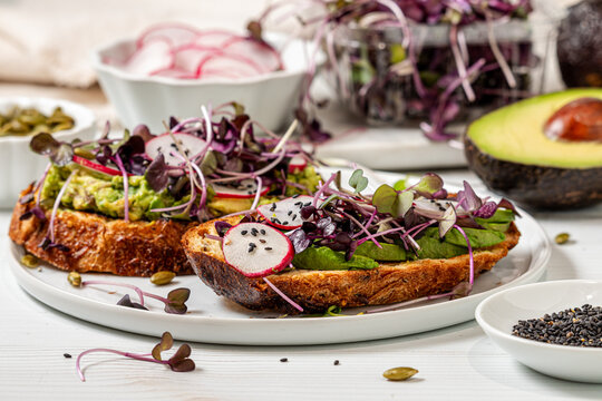Fresh and healthy avocado toast topped with microgreens and radish slices.