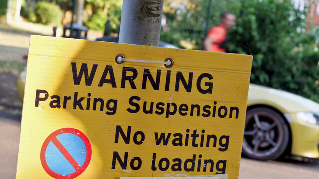 Parking suspension warning sign close up, yellow road notice with no waiting and no loading text, street restriction with blurred car and person background