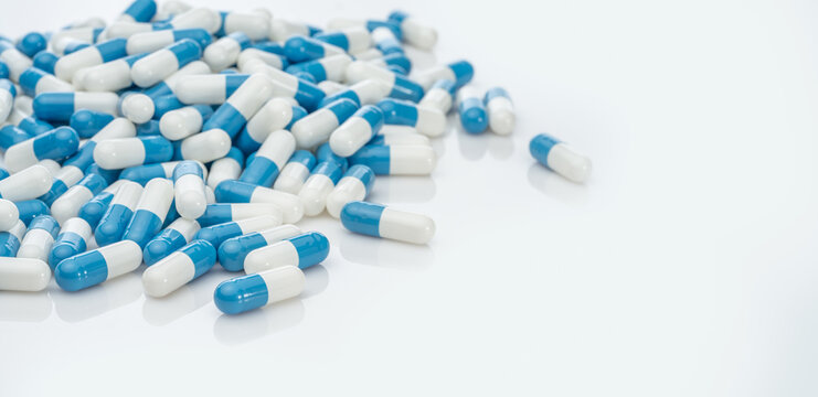 Blue-white antibiotic capsule pills on white background. Pile of antibiotic drug. Antibiotic drug resistance. Prescription drugs. Healthcare and medicine. Pharmaceutical industry. Pharmacy product.