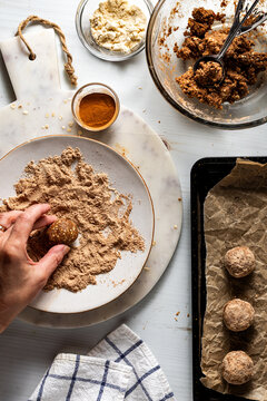 A hand coating an energy ball in a mixture of cinnamon and protein powder.