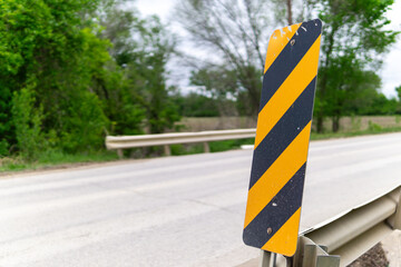 Close up of a yellow and black striped object marker sign near a section of collapsed road shoulder © David
