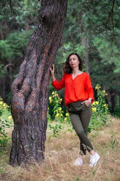 Woman in Red Blouse Leaning on Tree in Forest