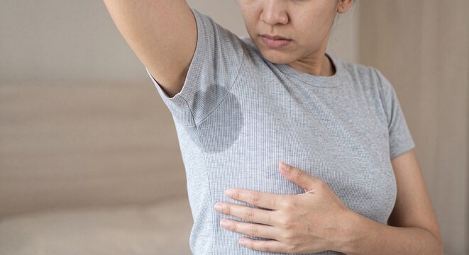 Asian woman looking at large sweat stain under armpit on grey t-shirt due to hyperhidrosis or hot weather