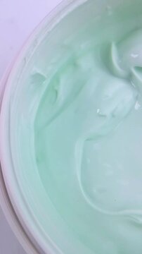 Top view of bright green whitening cream inside a white container. Beauty product presentation, smooth thick texture for skincare treatment.