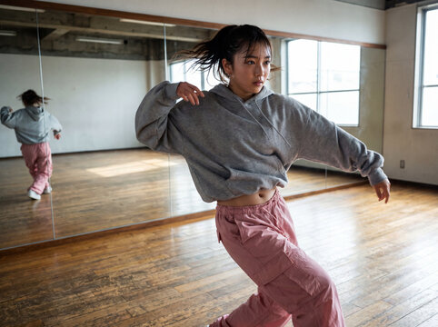 鏡張りのダンススタジオで真剣に練習するストリート系の女性ダンサー