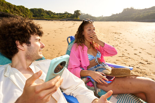 Happy couple reacting to smartphone content on beach vacation