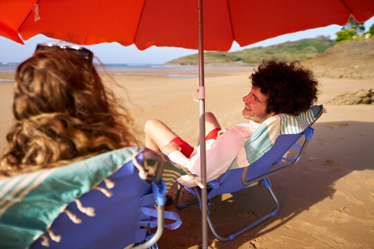 Couple relaxing on beach chairs under sun umbrella