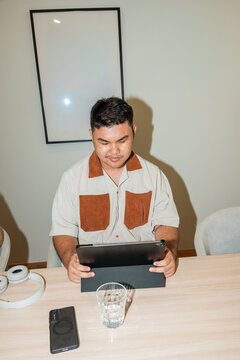 Young Asian Man Sits at Table Looking at Tablet in Office Setting