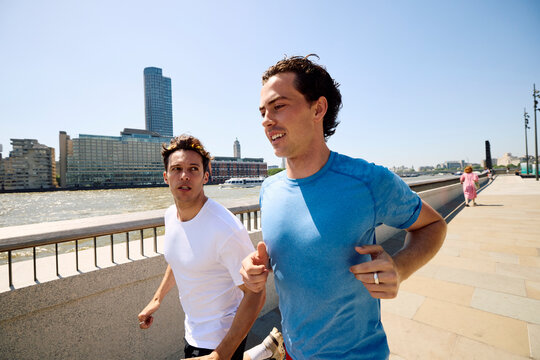Friends Run Along Riverside Path in London