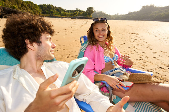 Young couple relaxing on beach chairs using smartphones