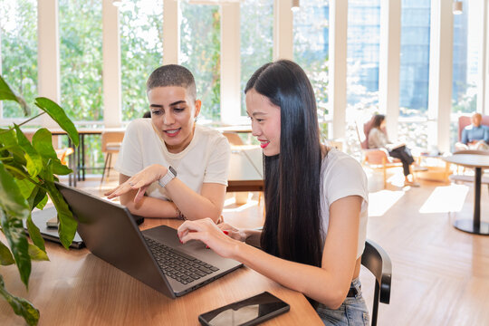 Two Women Talking and Working on a Laptop in a Modern Office Space