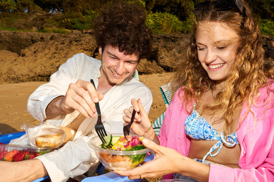 Young couple enjoying healthy poke bowl meal at beach picnic
