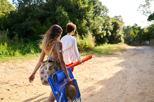 Couple walking on dirt path carrying beach gear